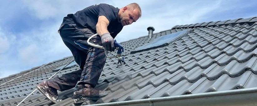 Mitarbeiter trägt eine professionelle Dachbeschichtung auf einem Ziegeldach auf
